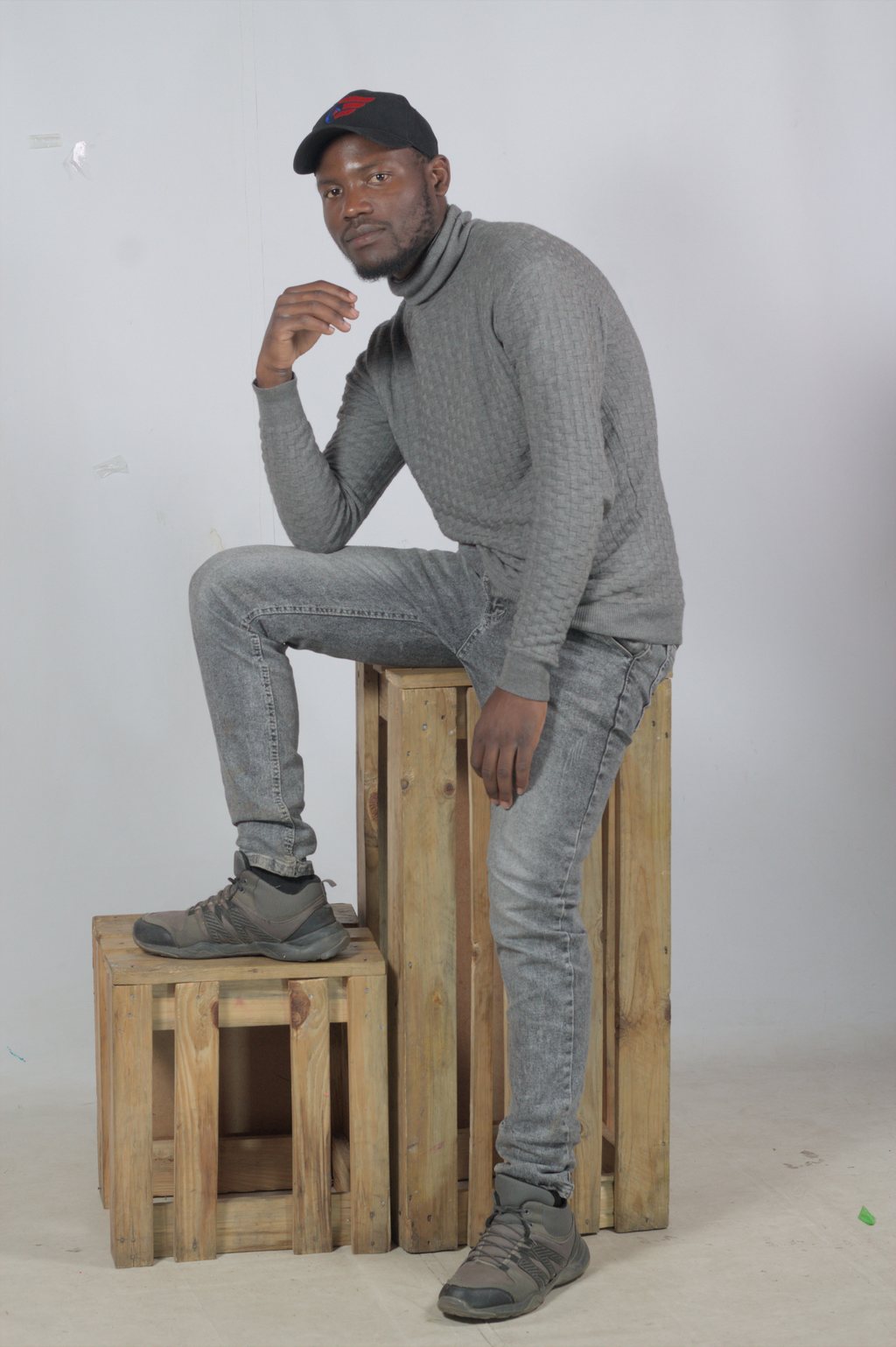 Portrait studio, homme en pull gris assis sur des caisses — raw file