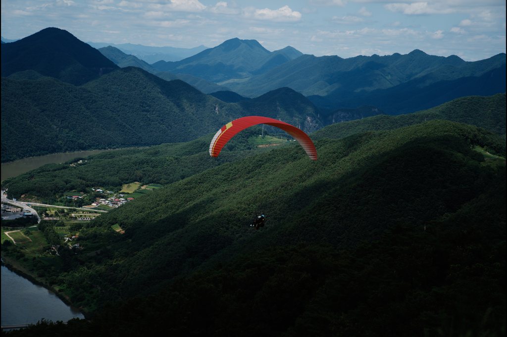 Parapente à voile rouge survolant des montagnes boisées et une vallée fluviale — neochrome version