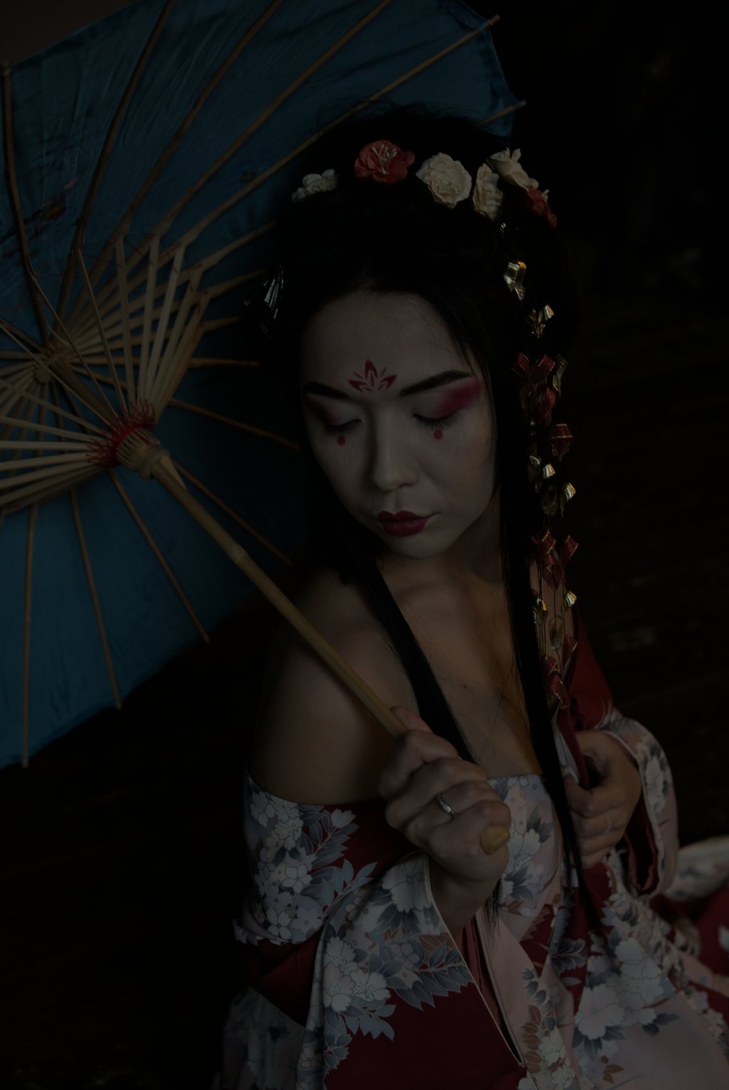 Portrait, jeune femme au maquillage et au kimono fleuri d'inspiration japonaise, ombrelle de papier bleue, lumière sombre — raw file