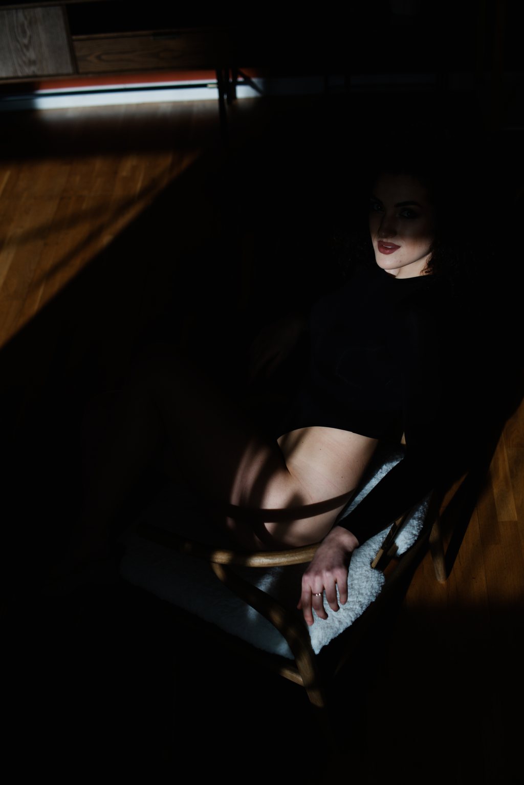 Portrait, femme aux cheveux bouclés assise sur une chaise, un rai de lumière traversant le parquet d'une pièce sombre — neochrome version