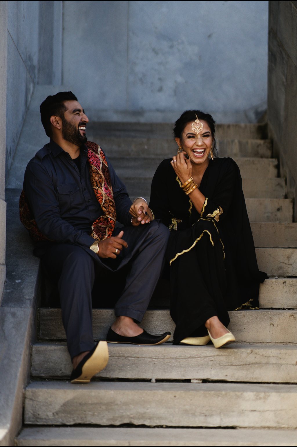 Couple riant assis sur des marches de pierre, tenues de fête indiennes brodées d'or — neochrome version