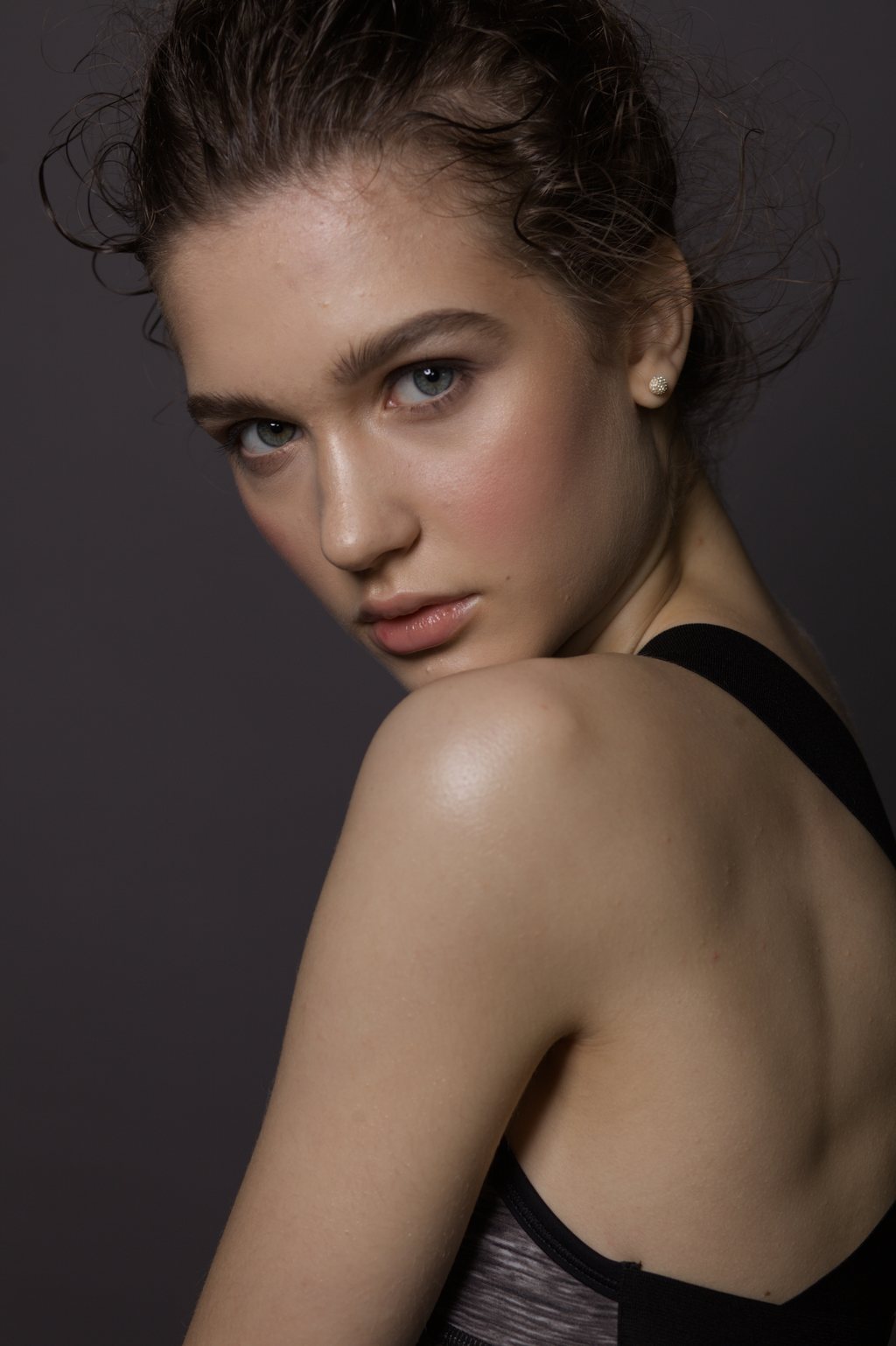 Portrait, jeune femme regardant par-dessus son épaule nue, teint lumineux, sur fond sombre — raw file