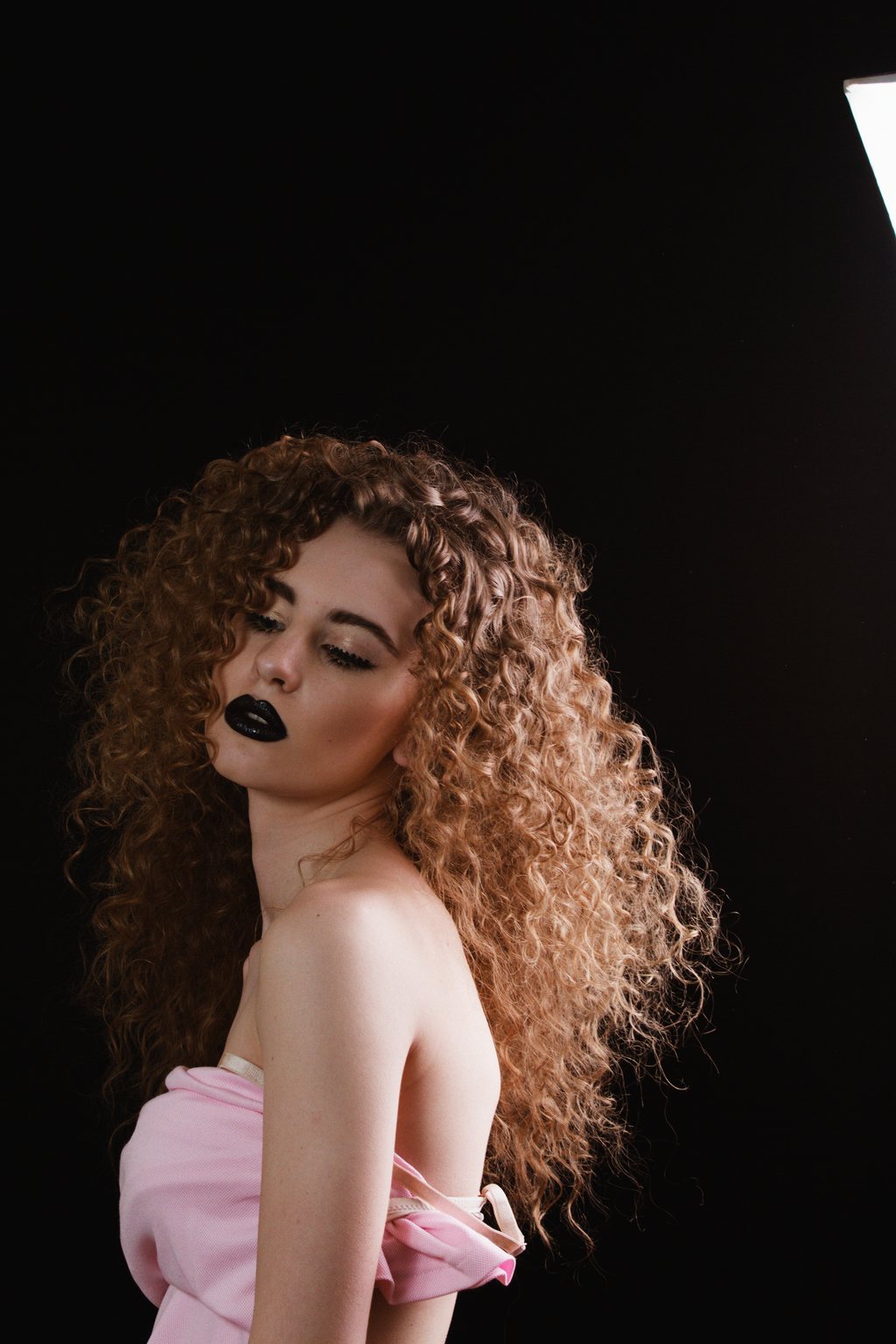 Portrait studio, jeune femme aux cheveux bouclés volumineux, rouge à lèvres noir, bustier rose sur fond noir — neochrome version